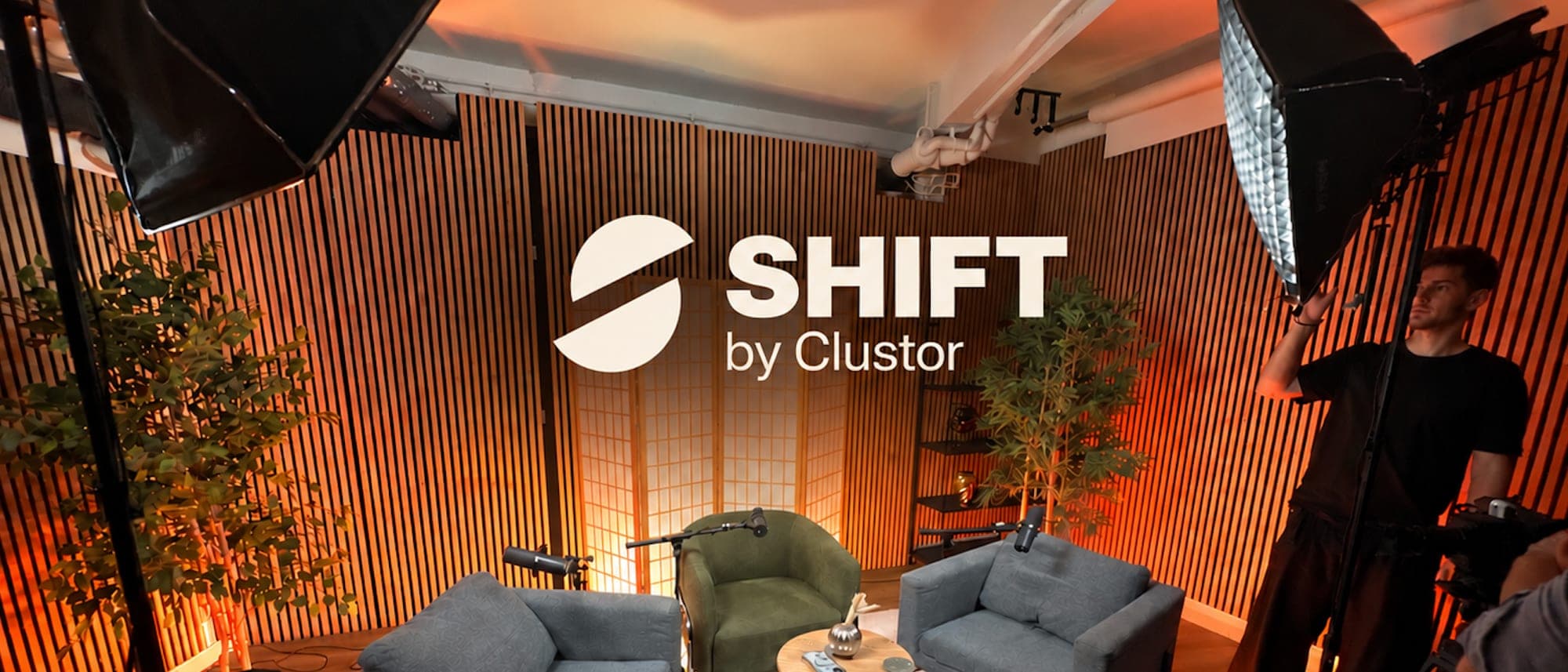 Le plateau de SHIFT by Clustor pendant les réglages lumière : deux fauteuils et une table basse face au mur de bois, sous une lumière orange